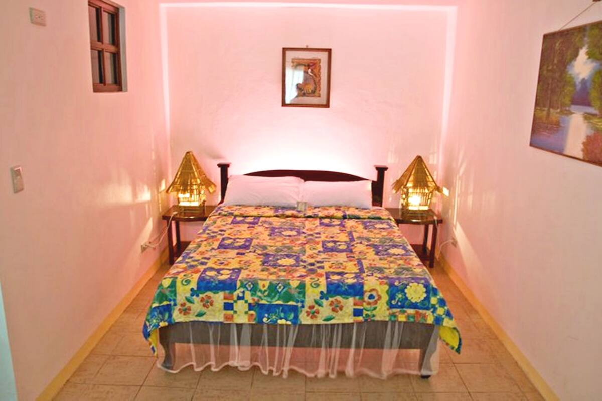 A bedroom with a bed, two bedside lamps, a window, and a painting on the wall.