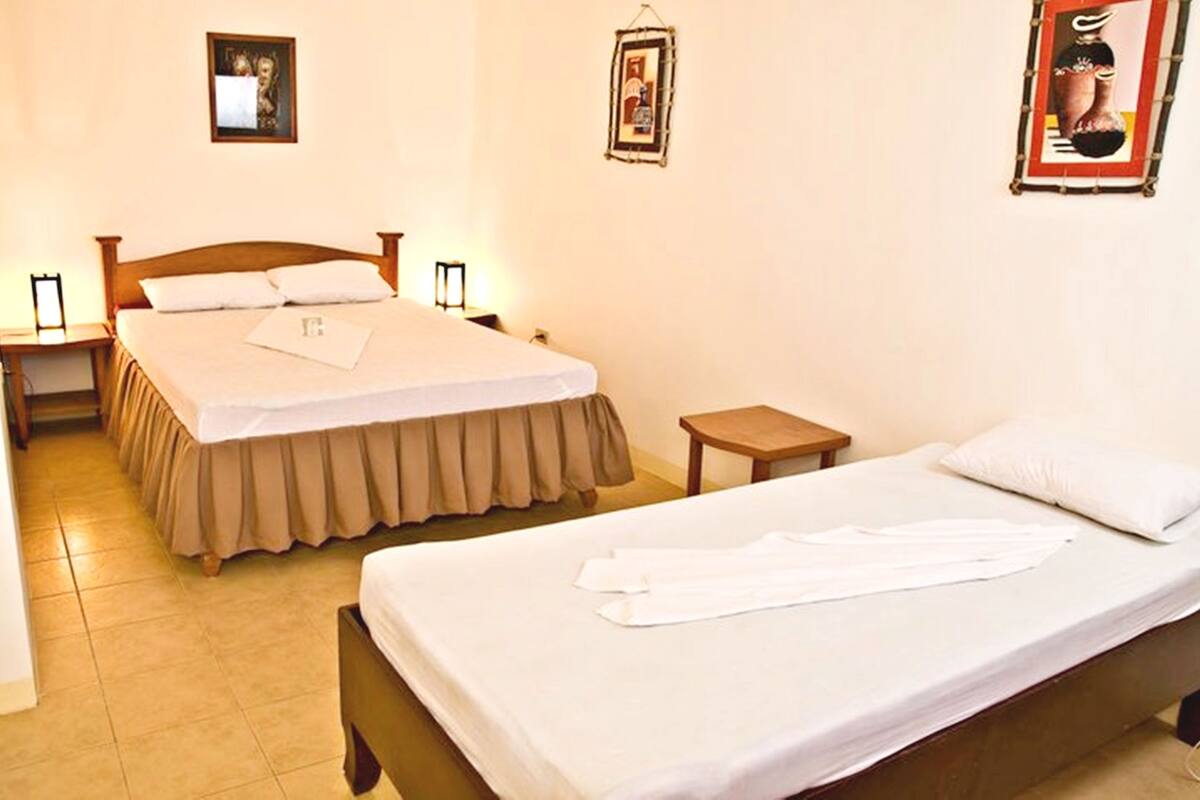 A hotel room with a large bed, a smaller bed, a nightstand, and a bedside table.