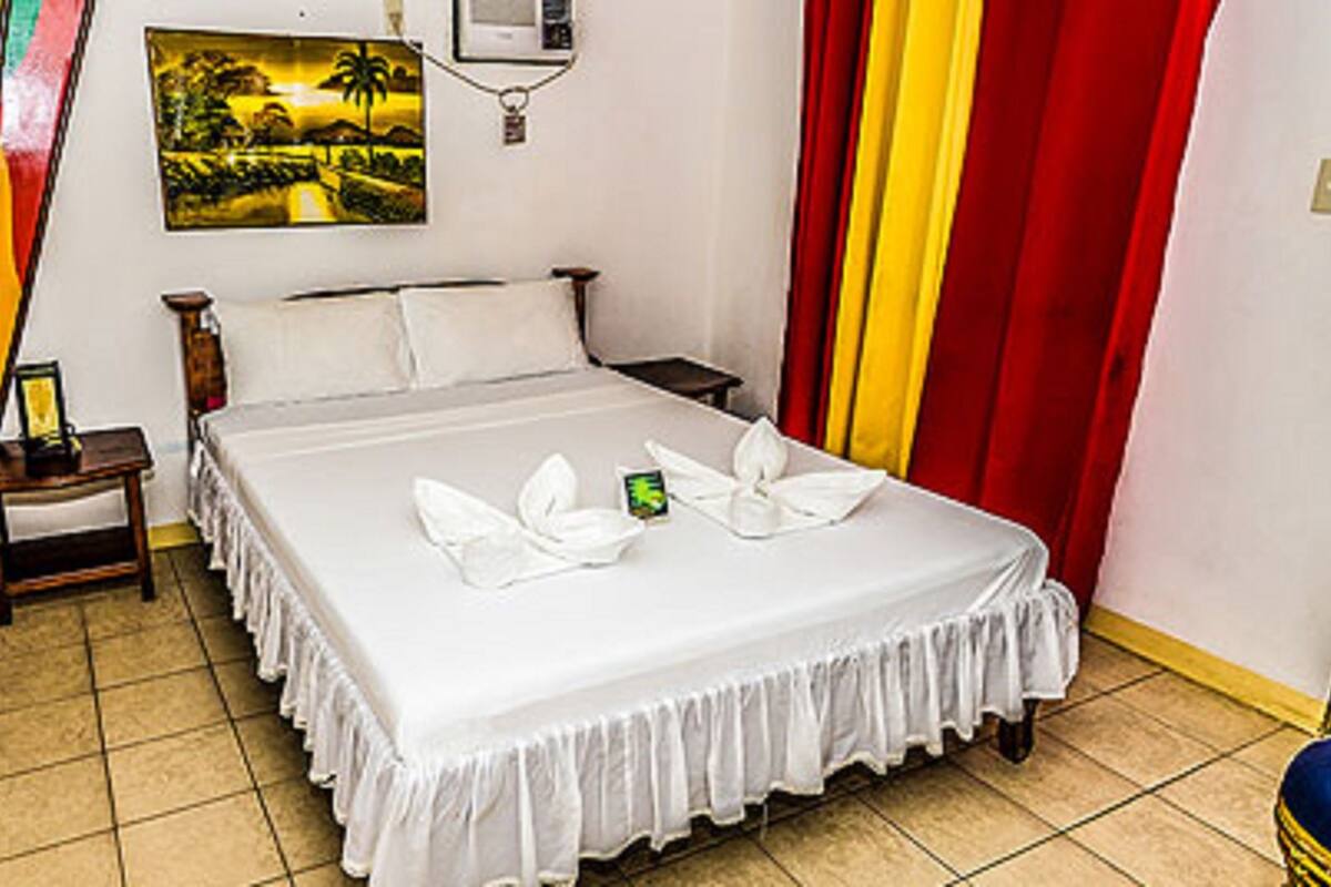 A neatly made bed with white linens and towels, a small bedside table with a lamp, and a painting on the wall.