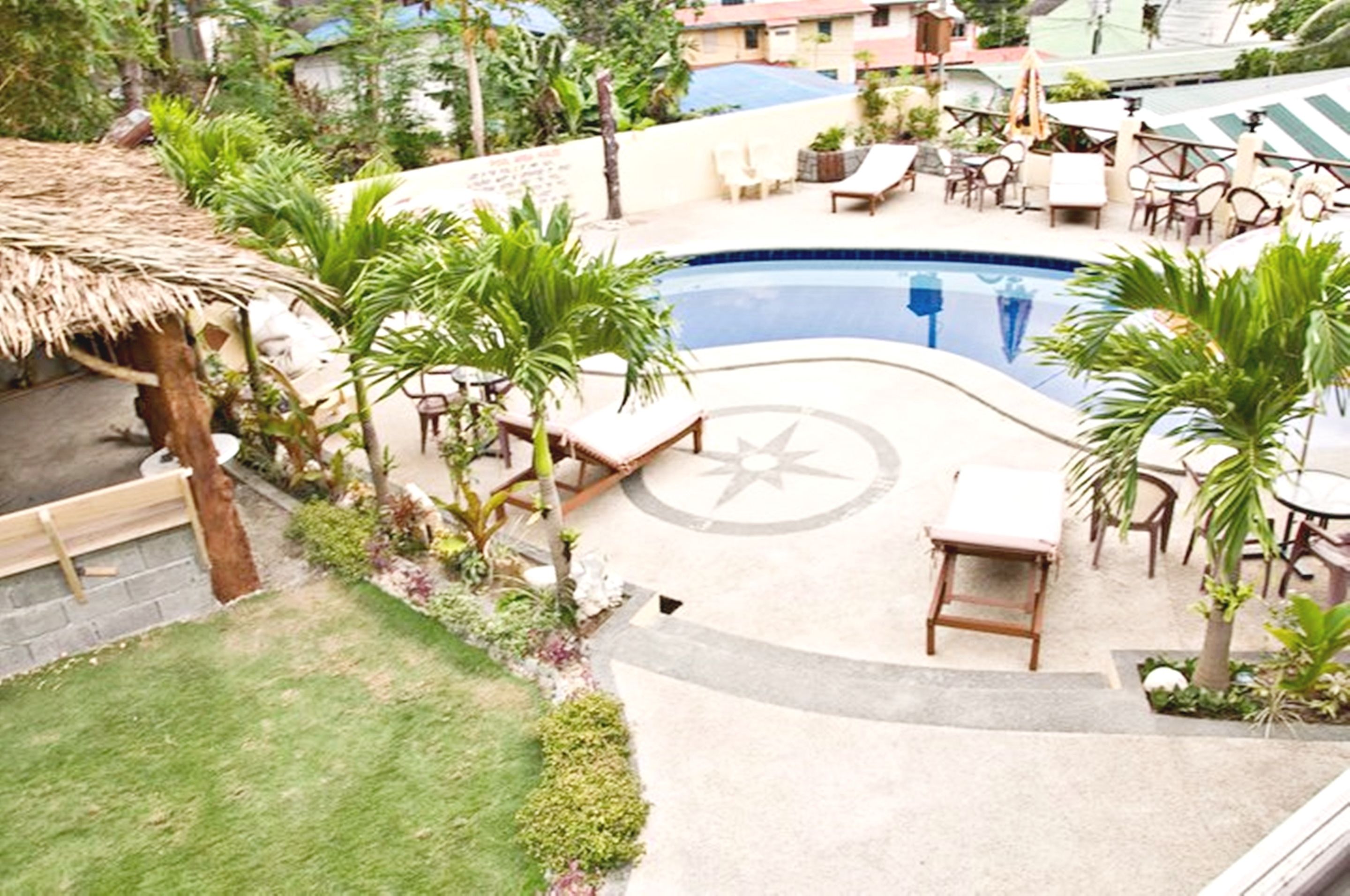 A pool area with lounge chairs, a thatched roof structure, and surrounding greenery.