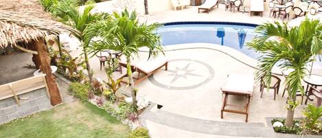 A pool area with lounge chairs, a thatched roof structure, and surrounding greenery.