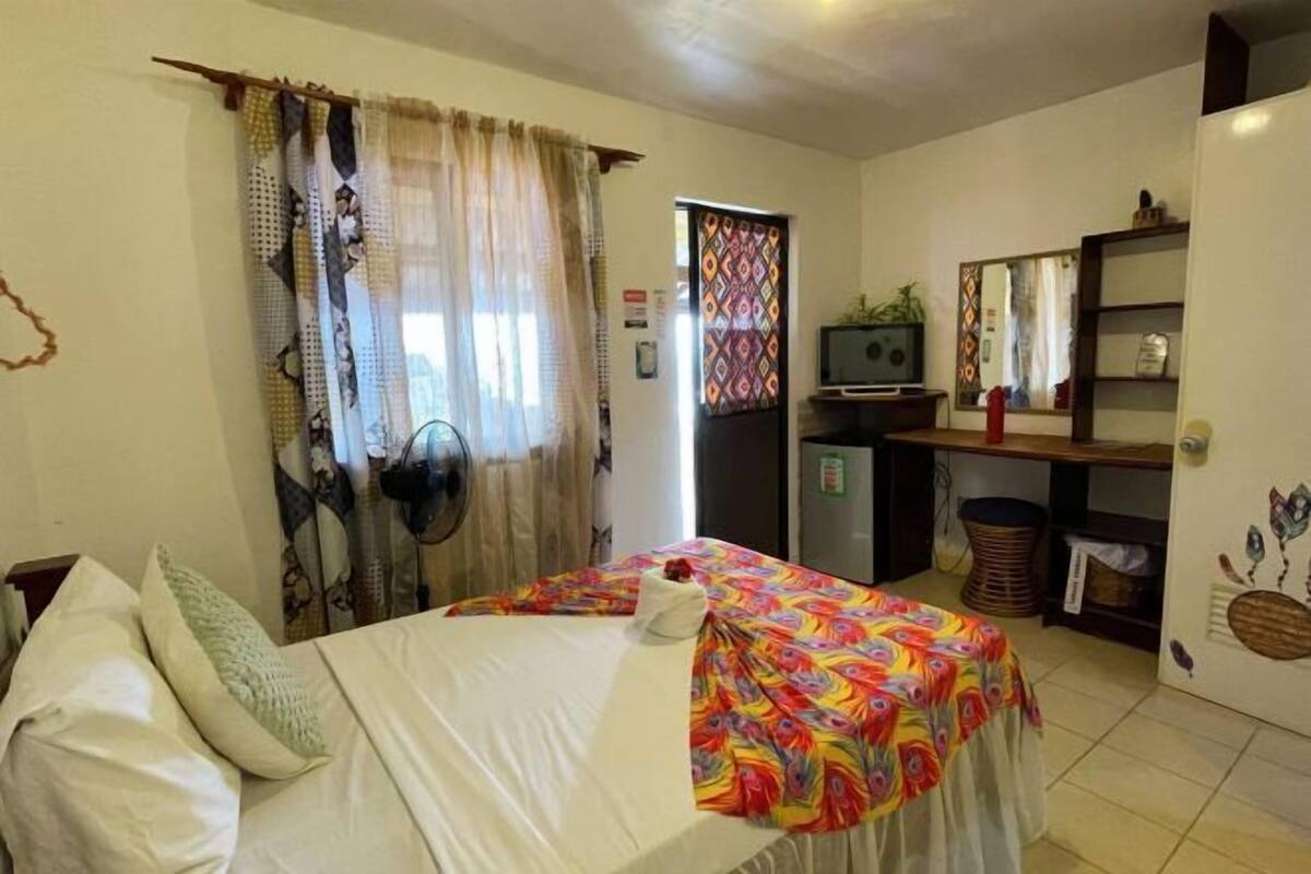 A bedroom with a bed, a desk, a chair, a TV, and a mirror.