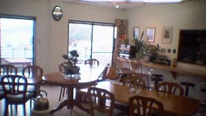 A dining area with wooden tables and chairs, a large window, and a wall-mounted speaker. - Seaside Uwakai (Seiyo)