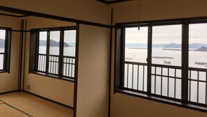 A room with tatami flooring, large windows with black frames, and a view of a body of water with distant mountains. - Seaside Uwakai (Seiyo)