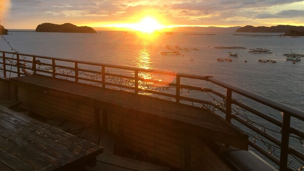 A sunset view from a wooden deck overlooking a body of water with boats and distant landforms. - Seaside Uwakai (Seiyo)