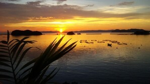 A sunset over a calm body of water with boats and distant landforms. - Seaside Uwakai (Seiyo)