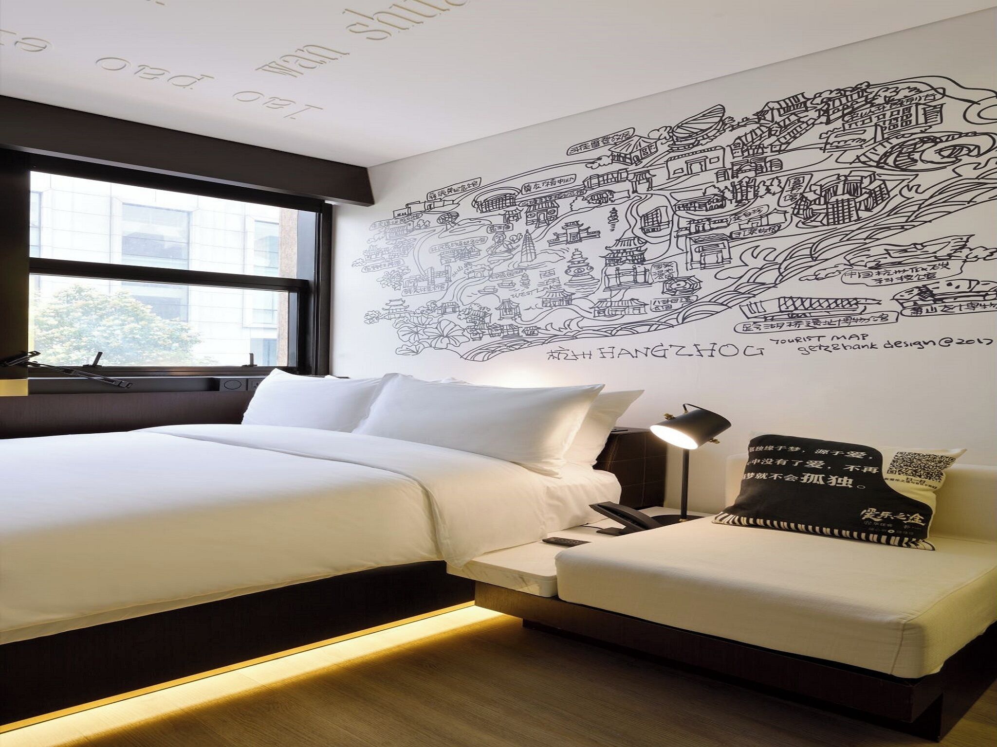 A hotel room with a large wall map, a bed, a bedside table, and a small sofa.