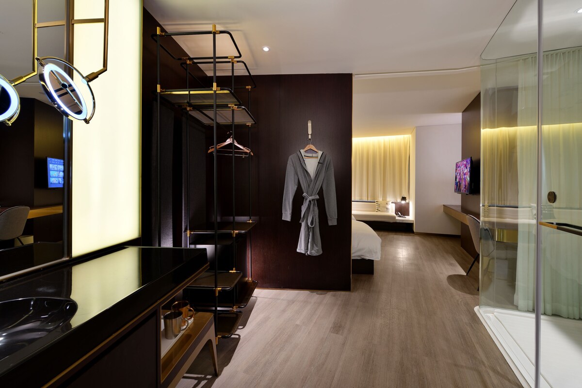 Una habitación de hotel moderna con tocador, bata, cama y separador de vidrio.