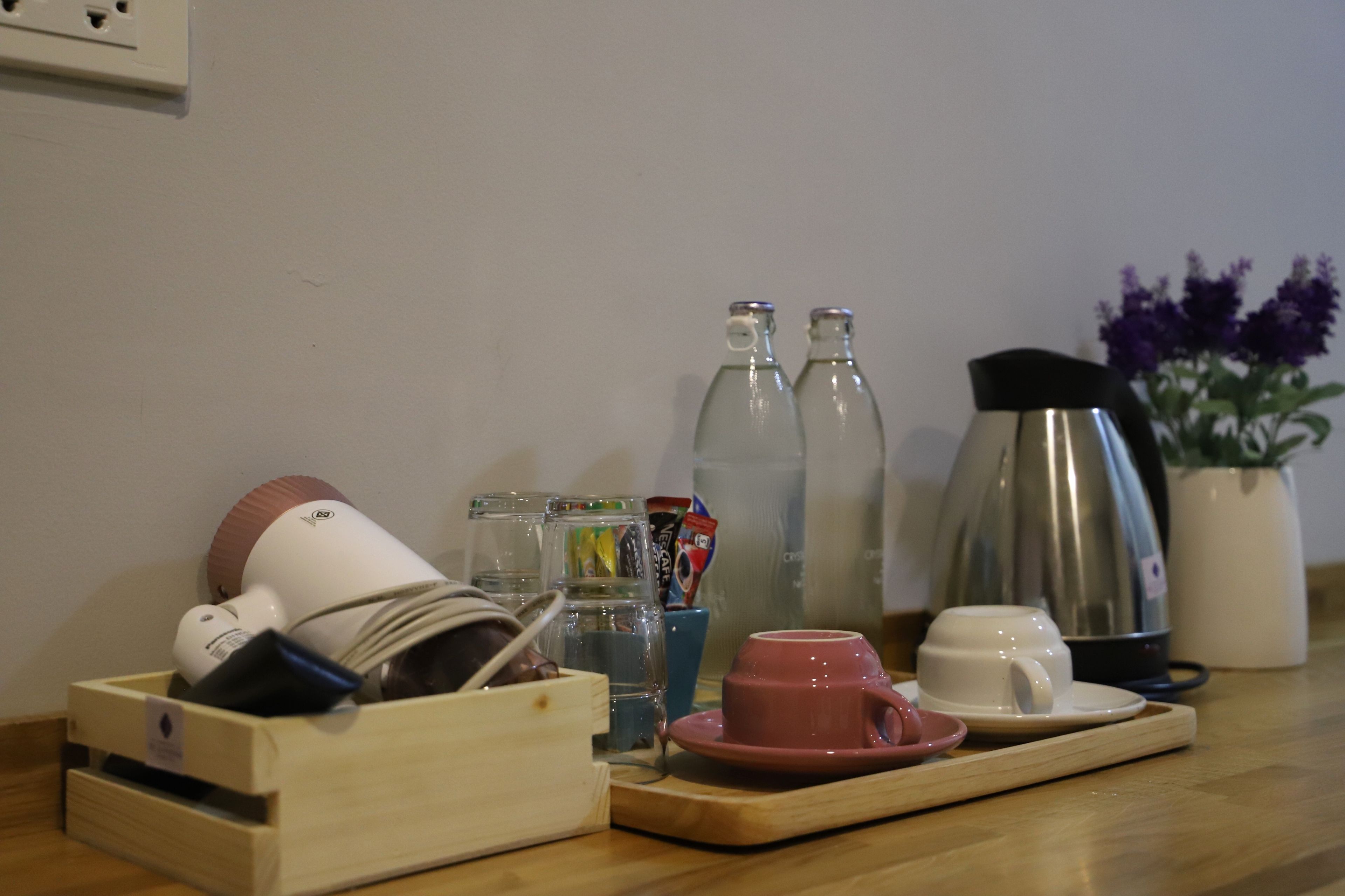 A kitchen counter with a coffee maker, a kettle, a tea kettle, a cup, a saucer, a tray, and a wooden box with utensils.