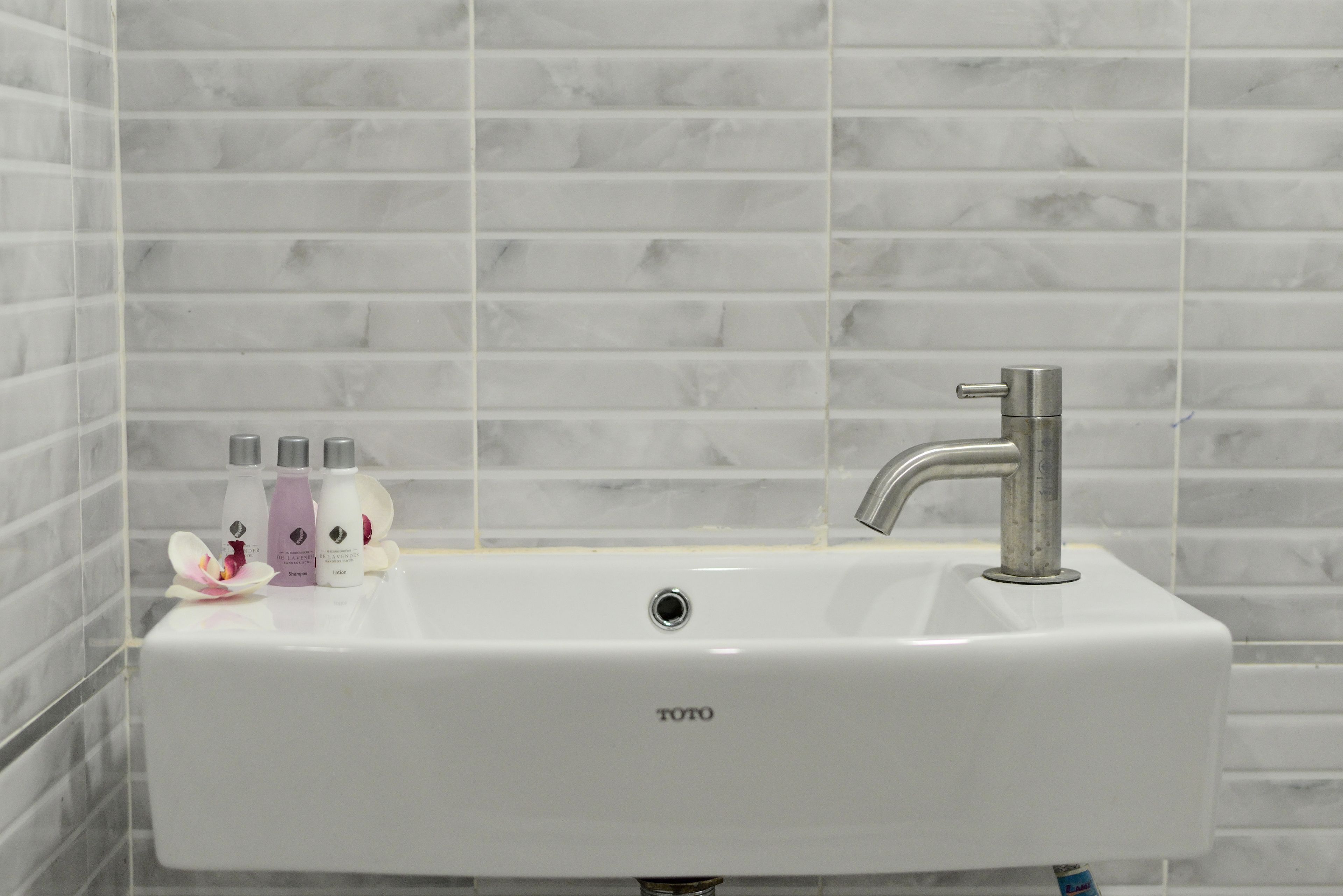 A white bathroom sink with a modern faucet, a TOTO brand label, and three bottles of lotion.