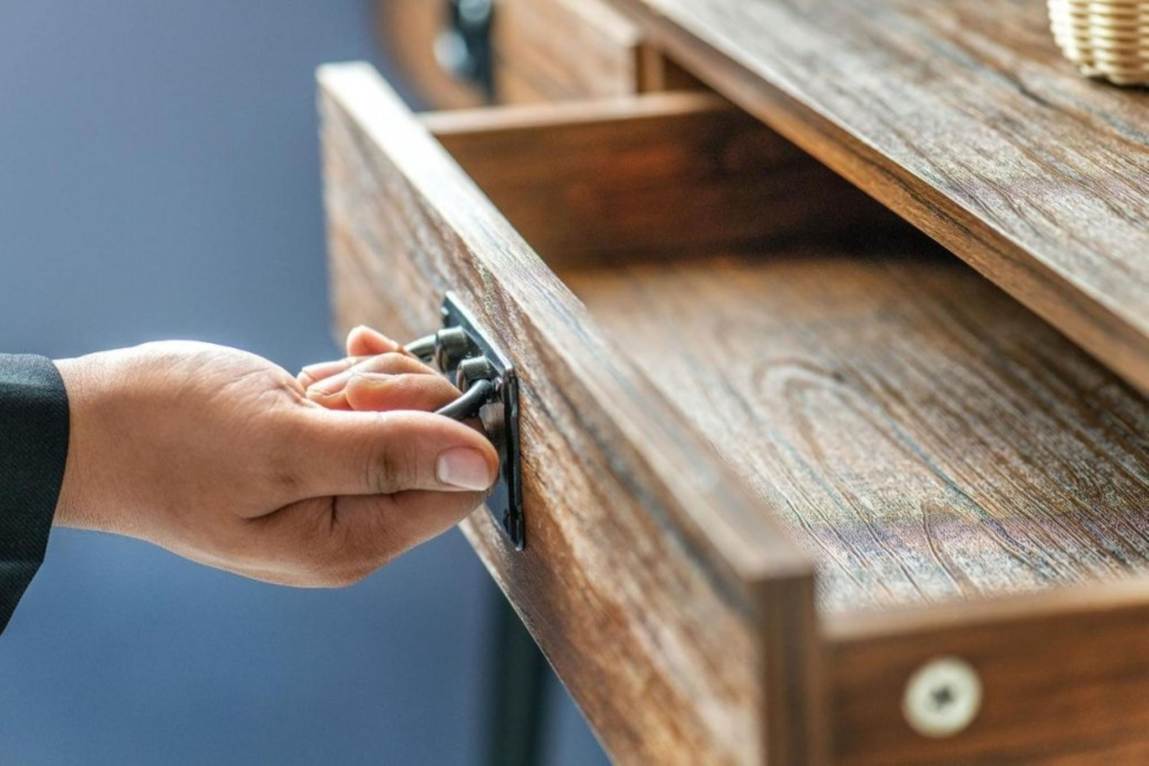 A hand pulling a drawer handle on a wooden piece of furniture.