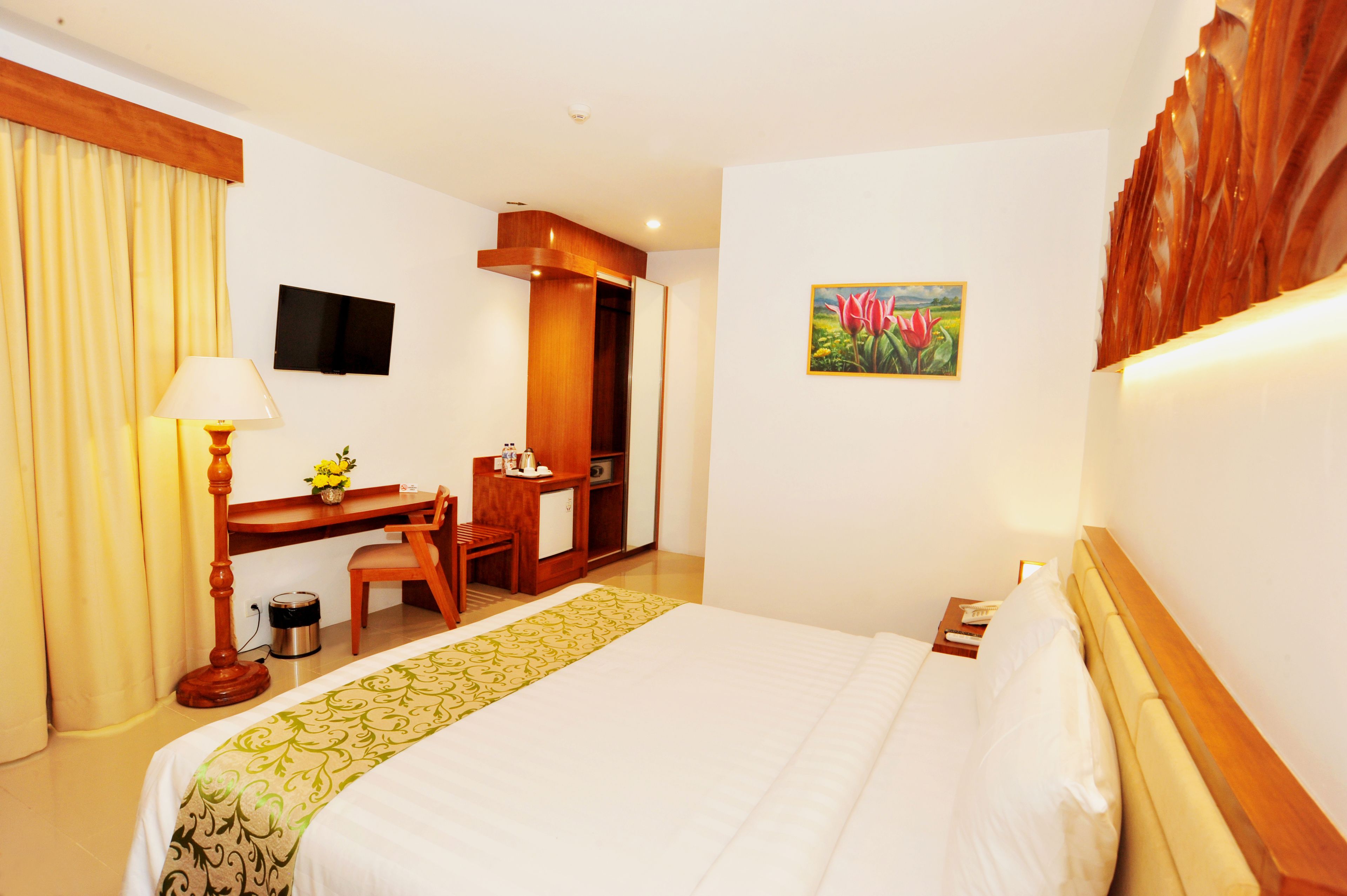 A hotel room with a bed, desk, chair, and a television on the wall.