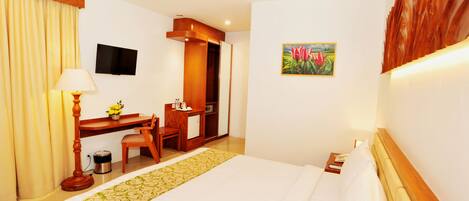 A hotel room with a bed, desk, chair, and a television on the wall.