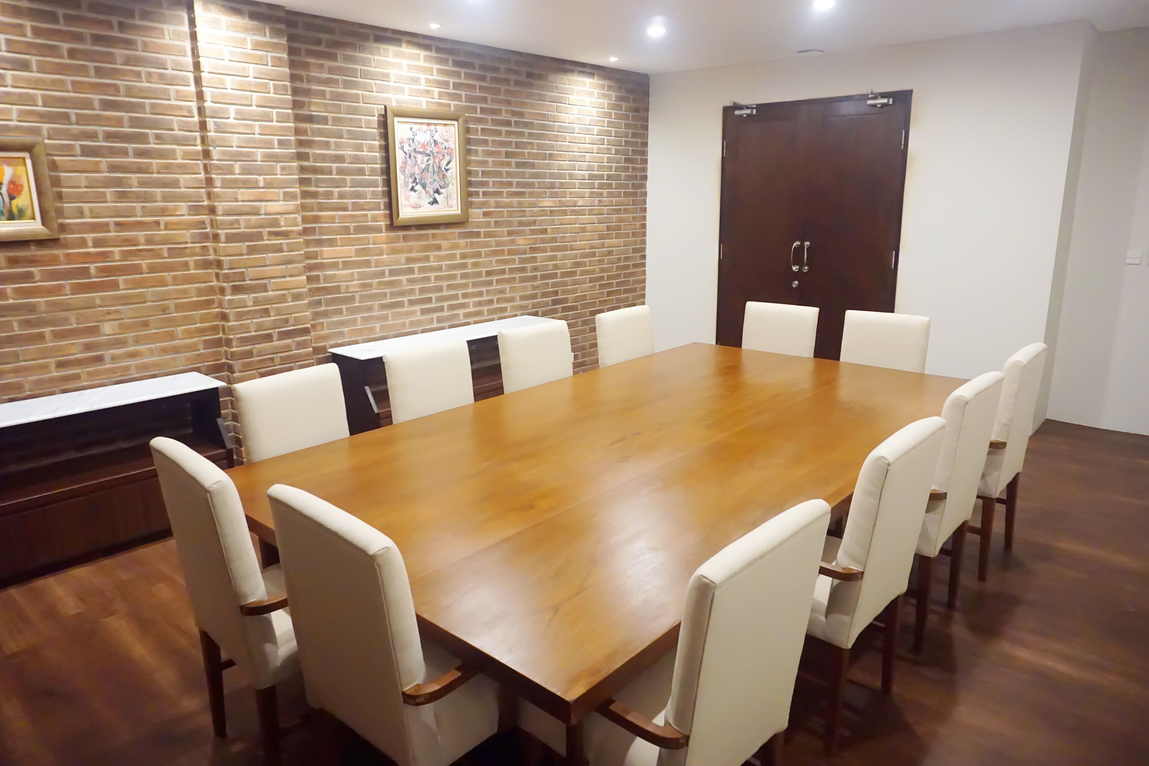A conference room with a wooden table and white chairs, brick wall, and a door.