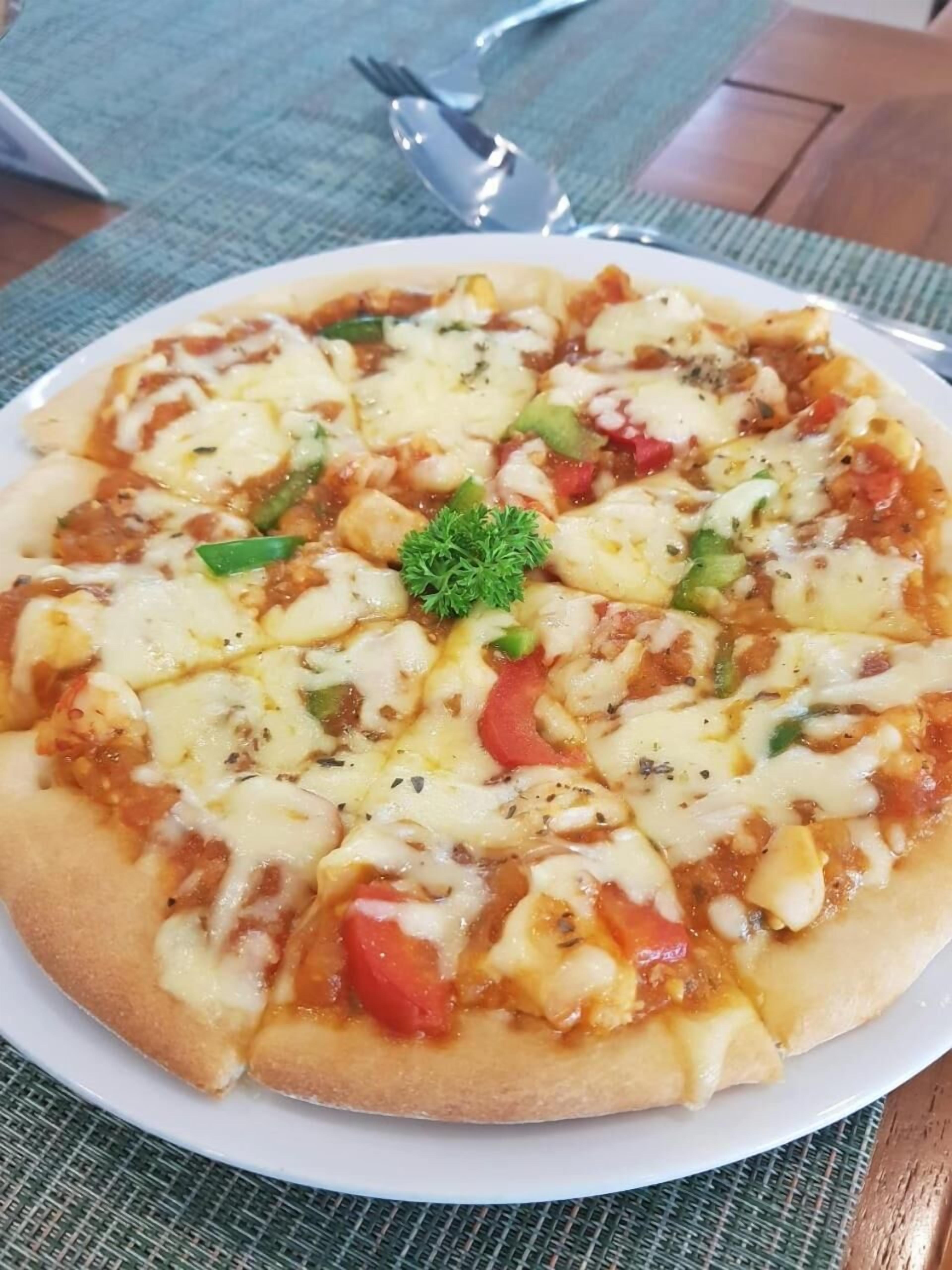 A pizza on a white plate with a green garnish, placed on a table with a woven placemat.