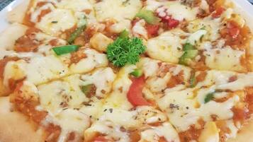 Pizza sobre un plato blanco con adorno verde, colocada sobre una mesa con un posavasos tejido.