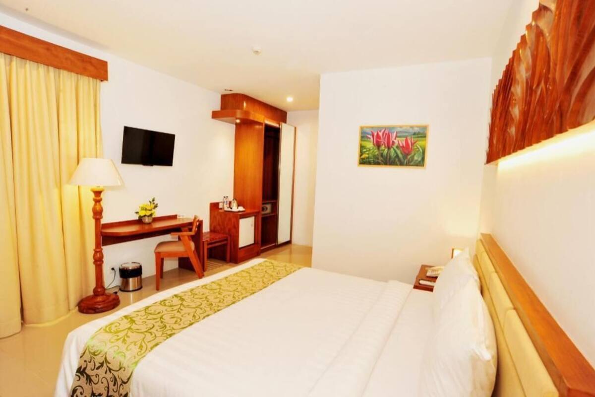 Ein Hotelzimmer mit Bett, Schreibtisch, Stuhl, Lampe, Fernseher und Kunstwerken.