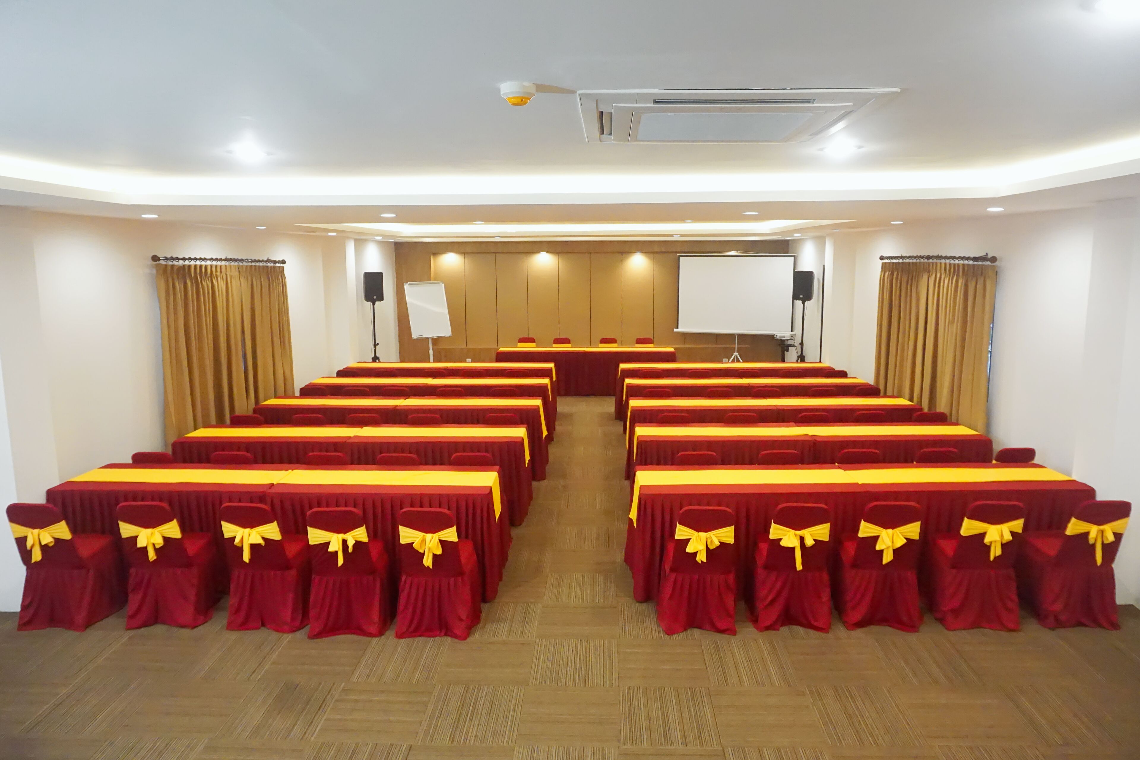Une salle de conférence avec des rangées de tables et de chaises, un tableau blanc et un écran de projection.
