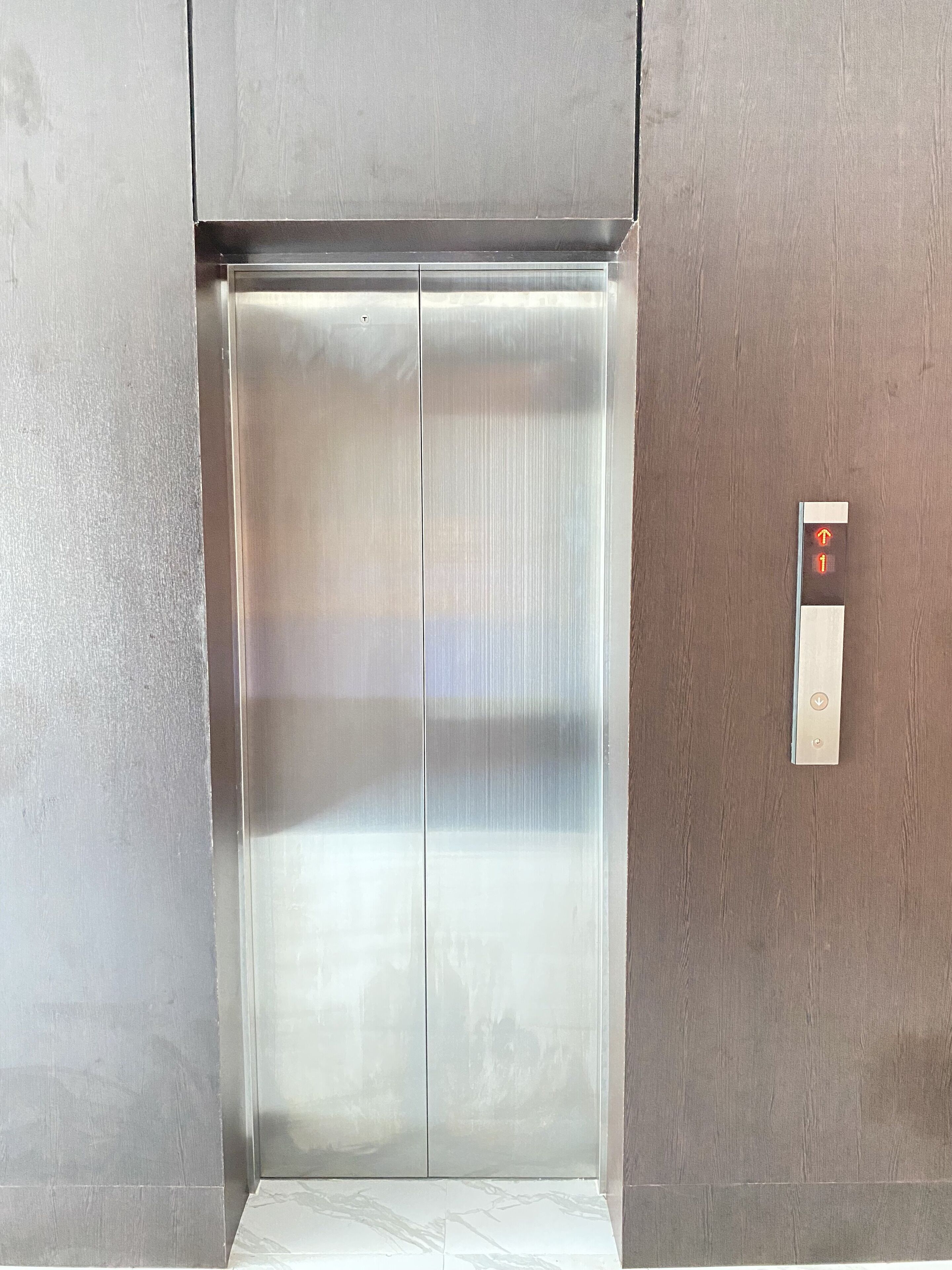 Um elevador moderno com acabamento metálico e painel de controle com setas indicando direções.