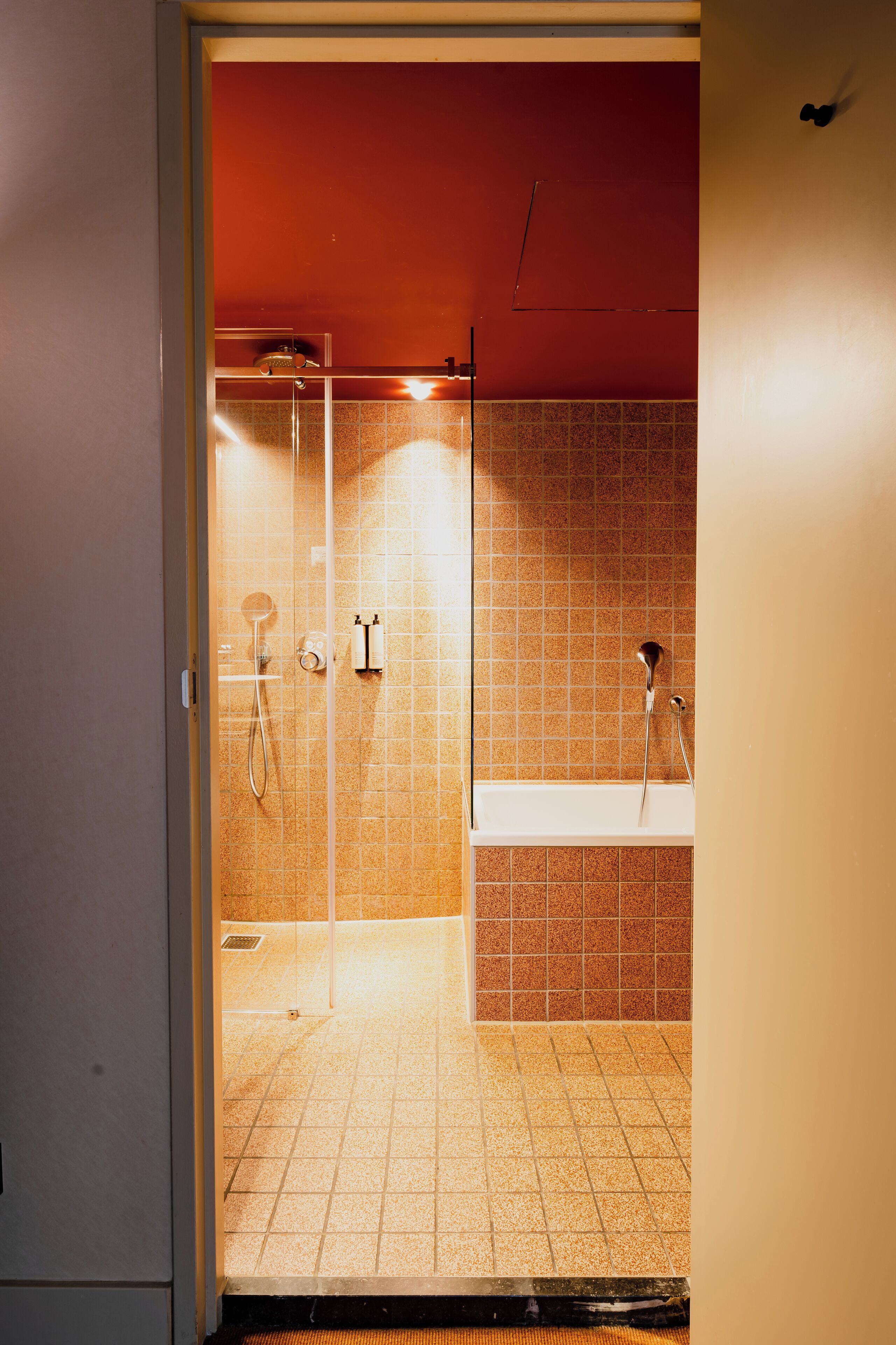 A bathroom with a glass shower enclosure, a white bathtub, and tiled walls.