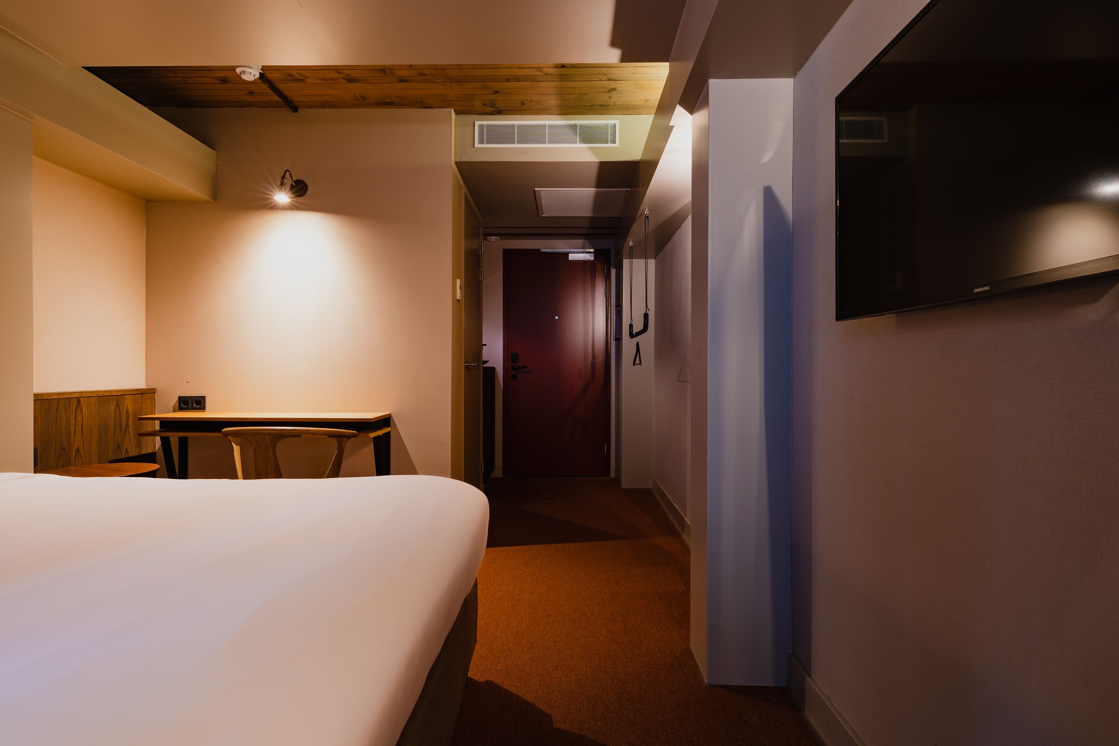 Hotelkamer met een bed, bureau, stoel, televisie aan de muur en een gang naar een andere kamer.