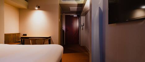 Hotelkamer met een bed, bureau, stoel, televisie aan de muur en een gang naar een andere kamer.