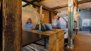 Een receptiebalie met een laptop, een vaas met gedroogde bloemen en een houten wand.