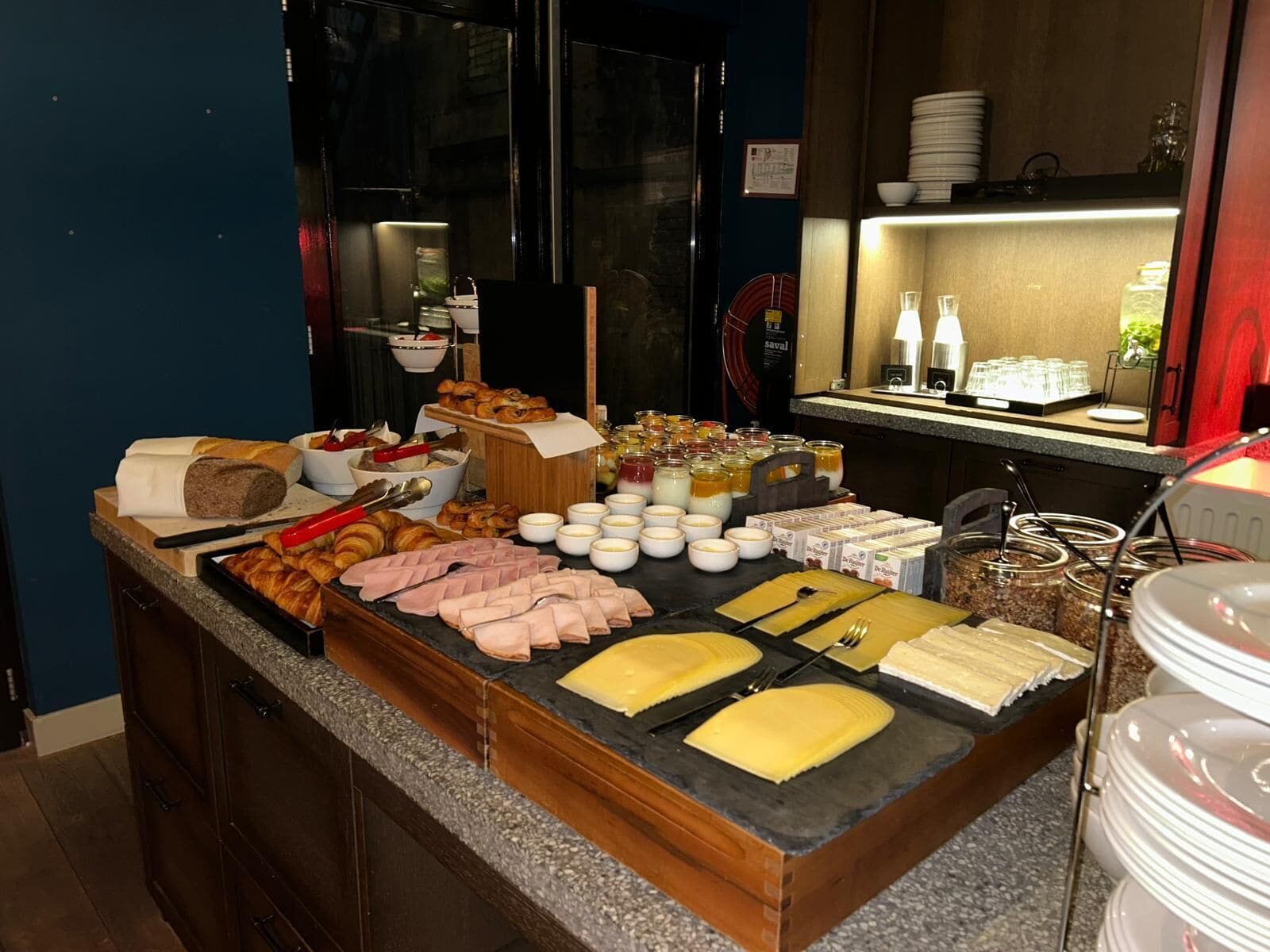 Montaje de bufé con diversos alimentos, como pan, pasteles y carnes, dispuestos en una barra.