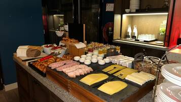 Montaje de bufé con diversos alimentos, como pan, pasteles y carnes, dispuestos en una barra.