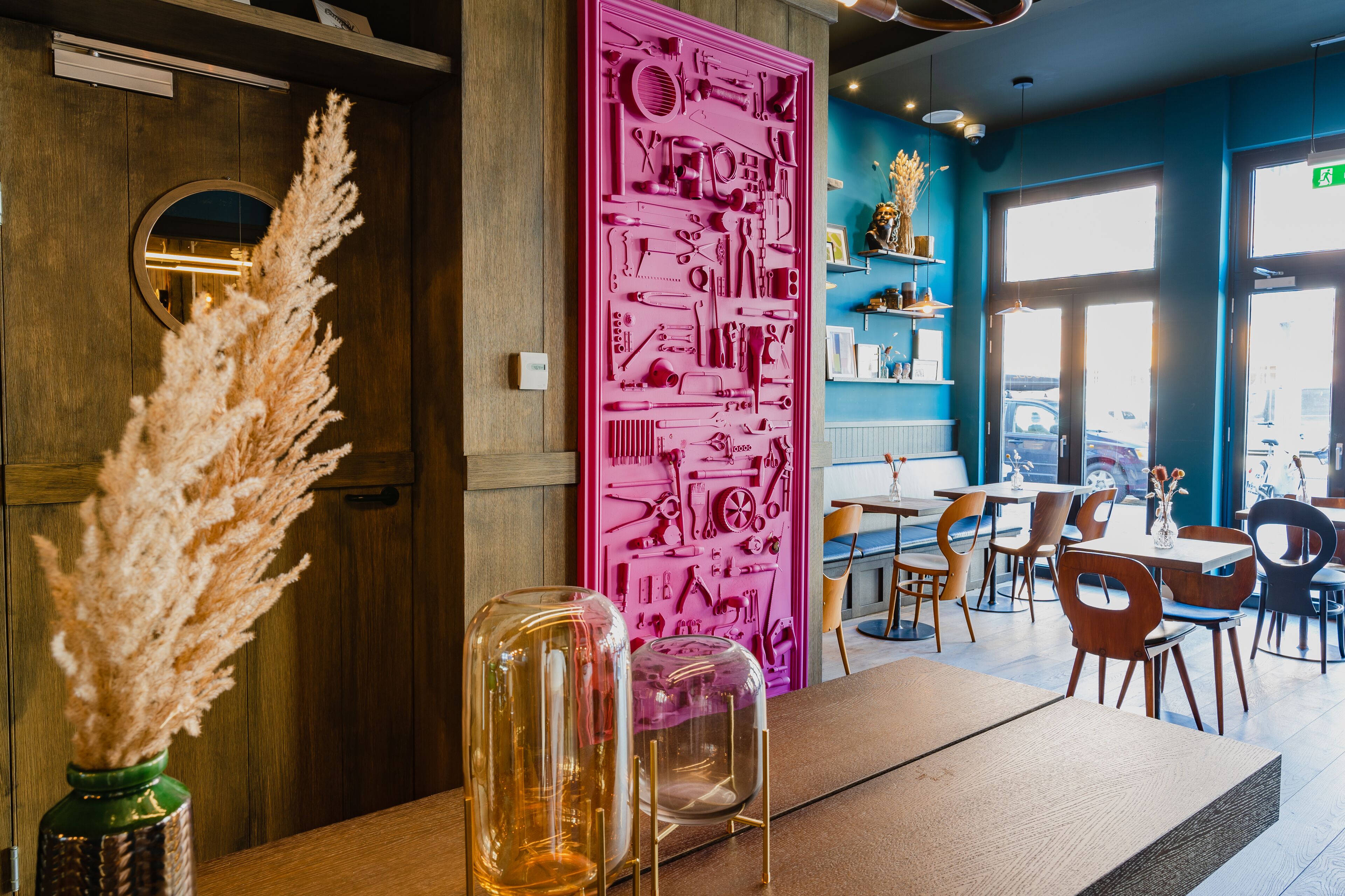 A restaurant interior with wooden paneling, a pink decorative panel, and a view of the street through large windows.