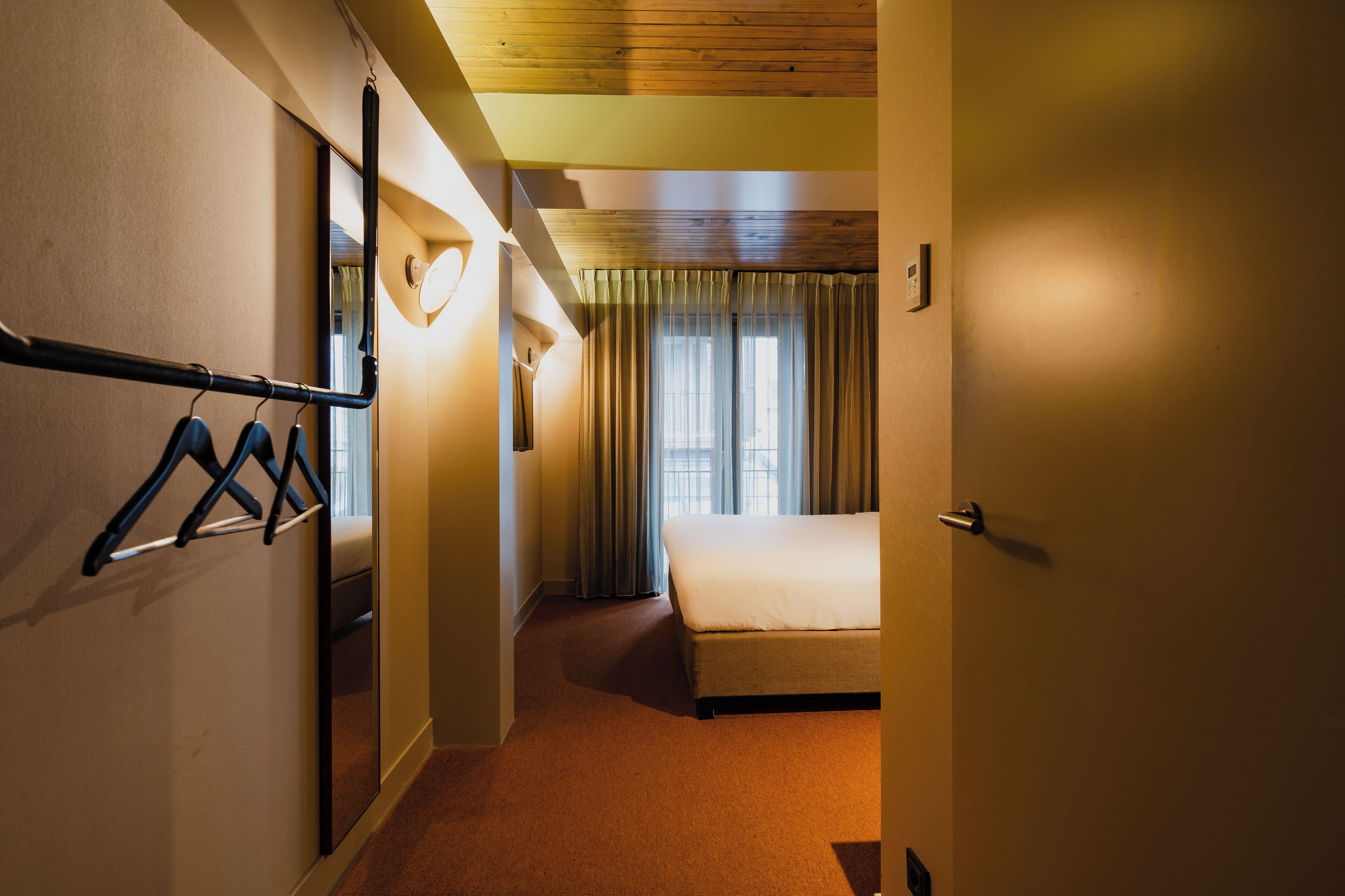 Una habitación de hotel con una cama, un espejo, un perchero y una puerta.