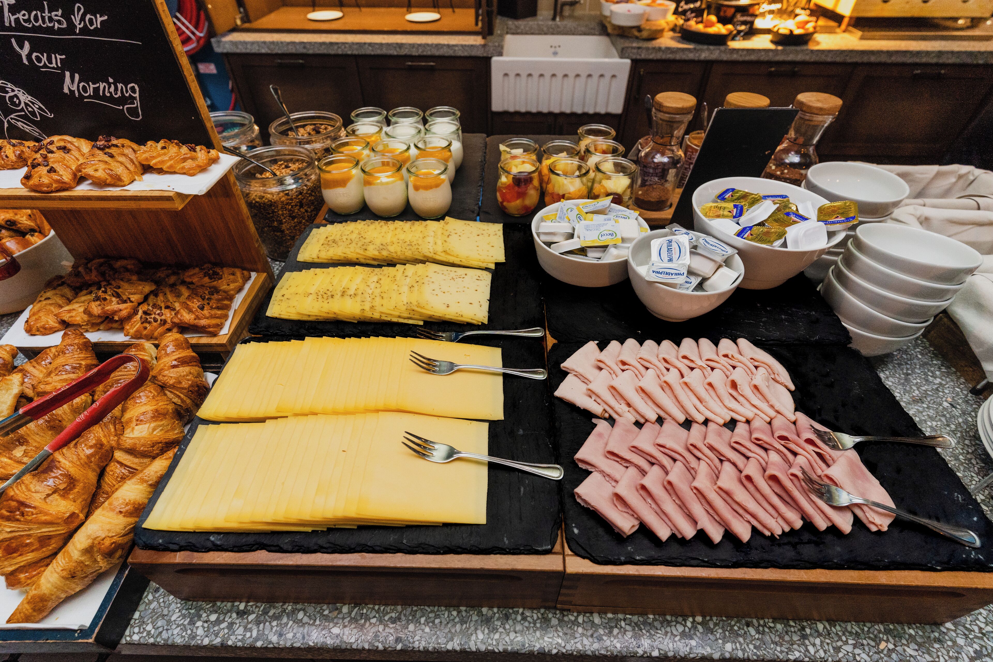 Een ontbijtbuffet met gebak, kaas, vleeswaren en diverse toevoegingen.