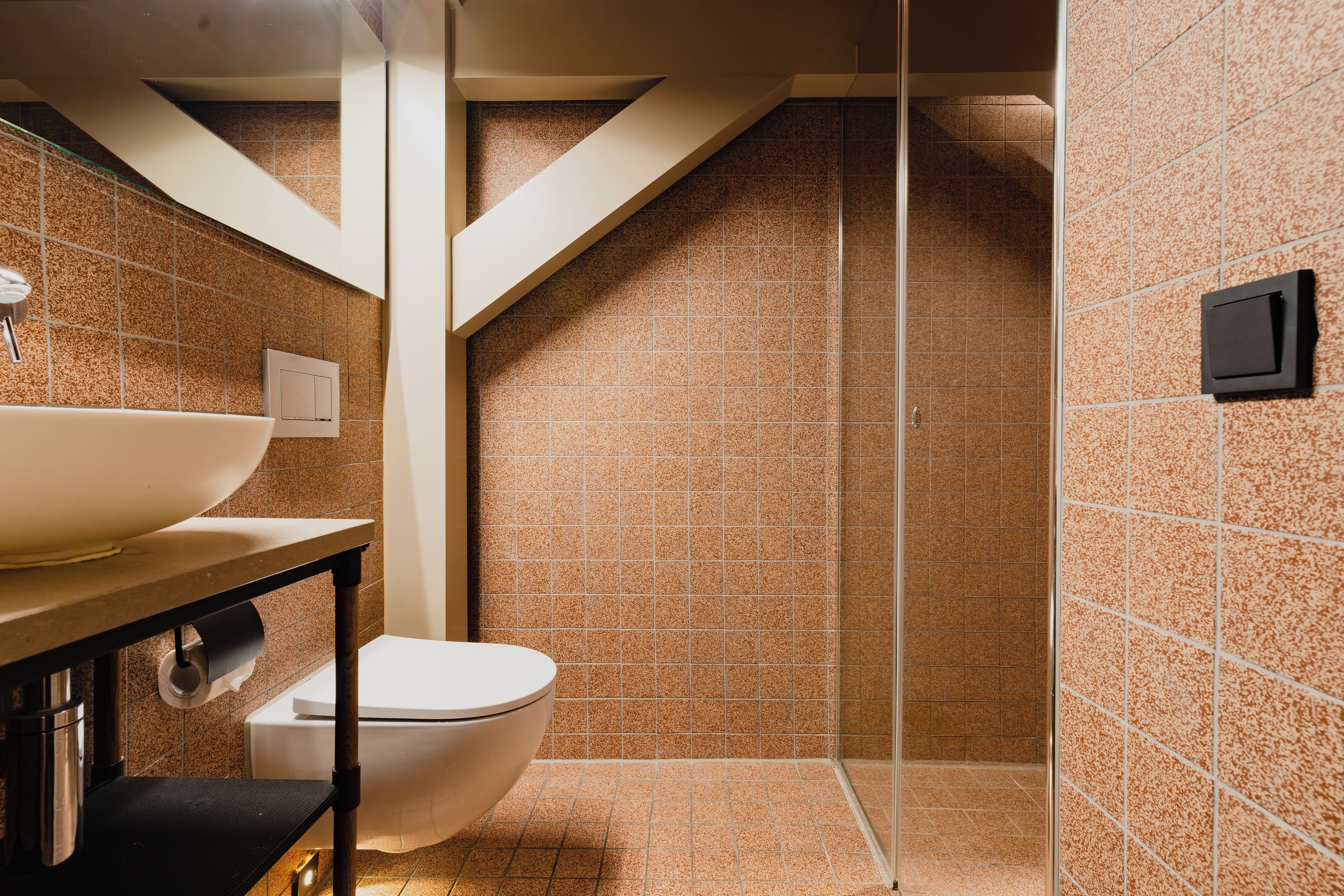 Un baño con inodoro blanco, lavamanos con recipiente amplio y zona de ducha con puerta de cristal.