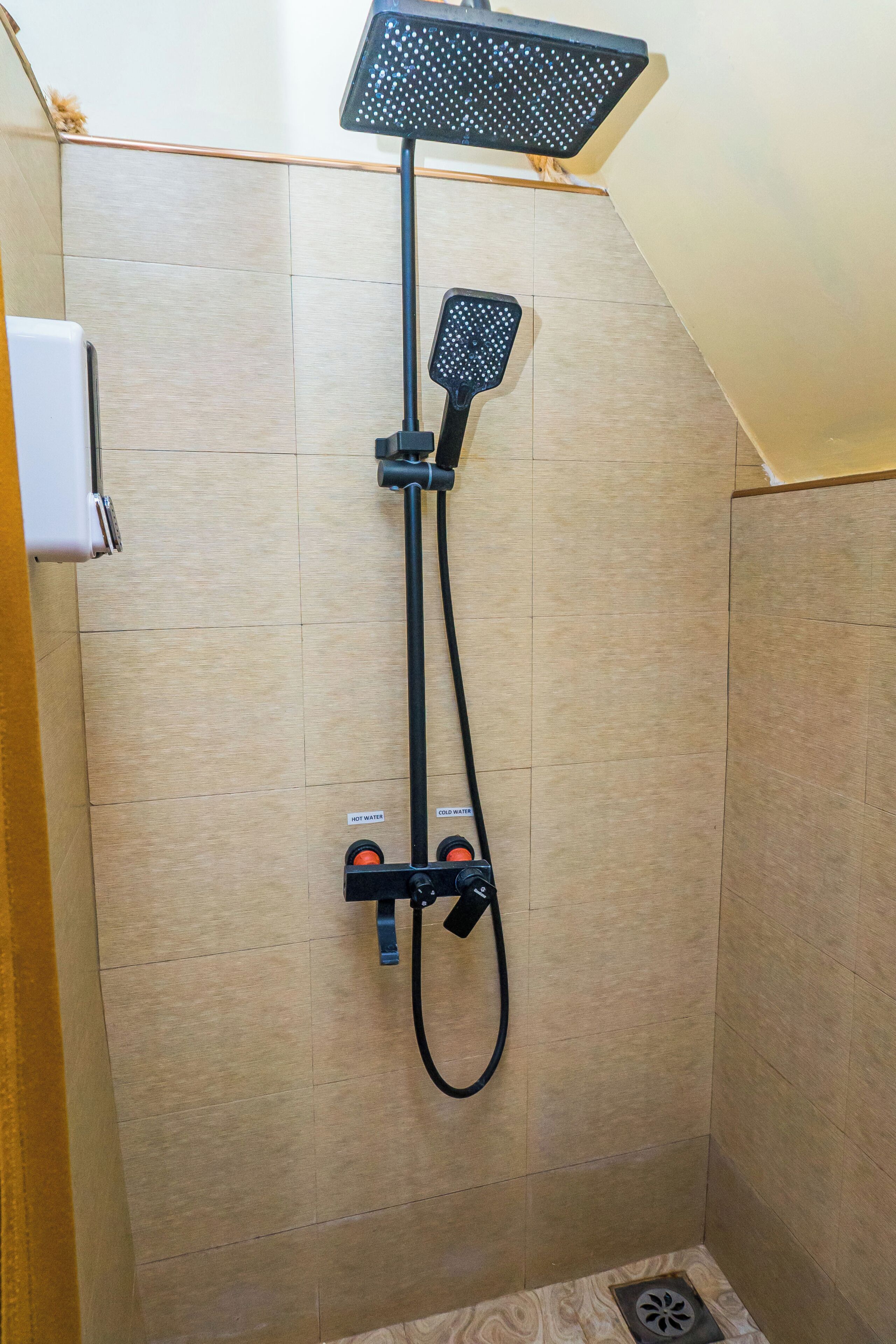 A shower with a handheld showerhead and a wall-mounted faucet. There are two control knobs labeled 'HOT WATER' and 'COLD WATER.'