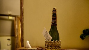 A bottle of champagne in a woven basket, a glass jar, and a candle holder on a table.