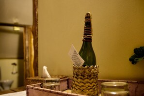 A bottle of champagne in a woven basket, a glass jar, and a candle holder on a table. - Karama Lodge & Spa (Arusha)