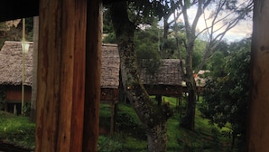 A view through a window of a rustic wooden structure with thatched-roof buildings in a lush, green landscape.