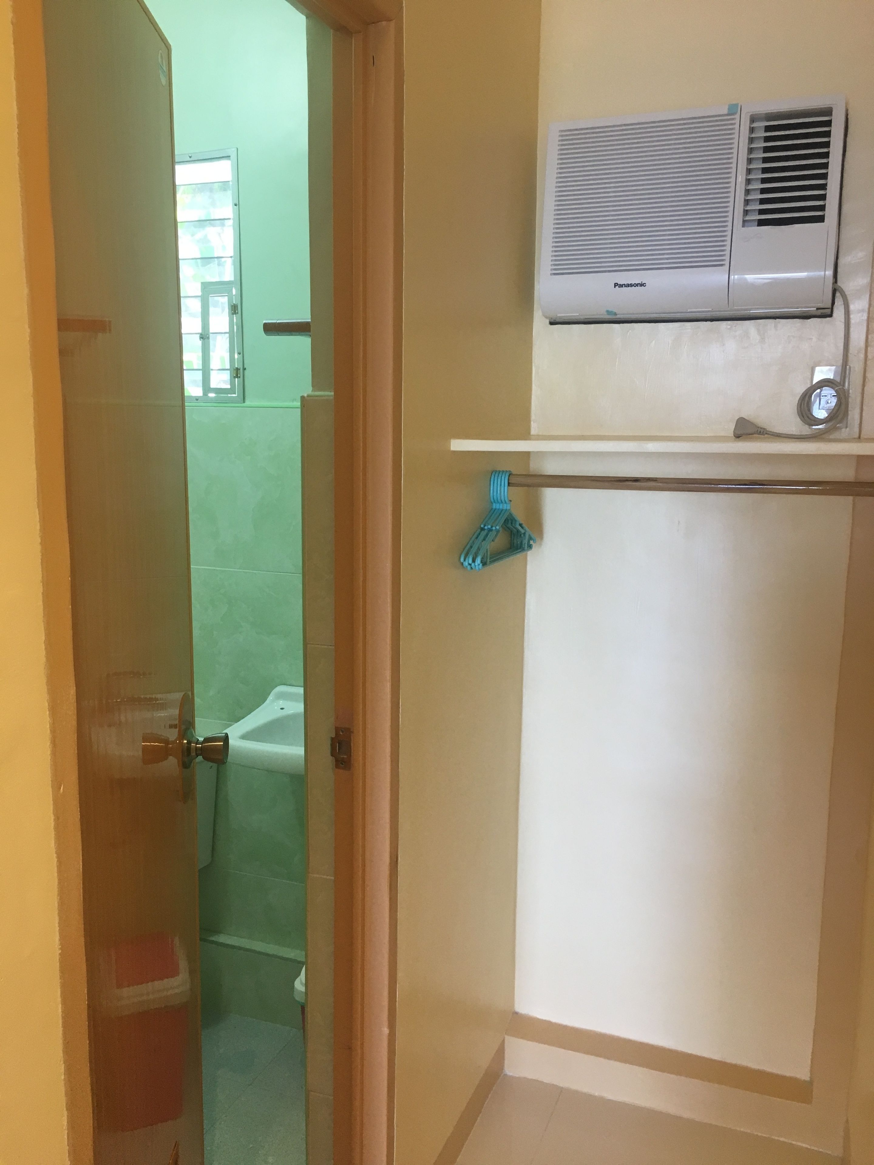 A room with a bathroom, a wall-mounted air conditioner, and a door with a towel rack.