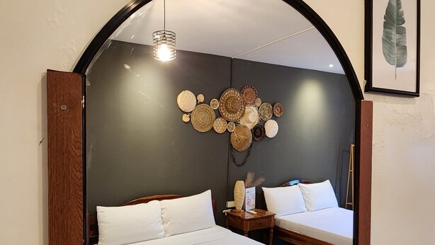 A bedroom with two beds, a mirror, a wall art piece, and a hanging light fixture.