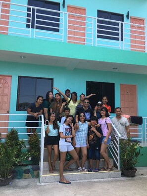 A group of people posing on a staircase in front of a building with a light blue facade and orange doors.