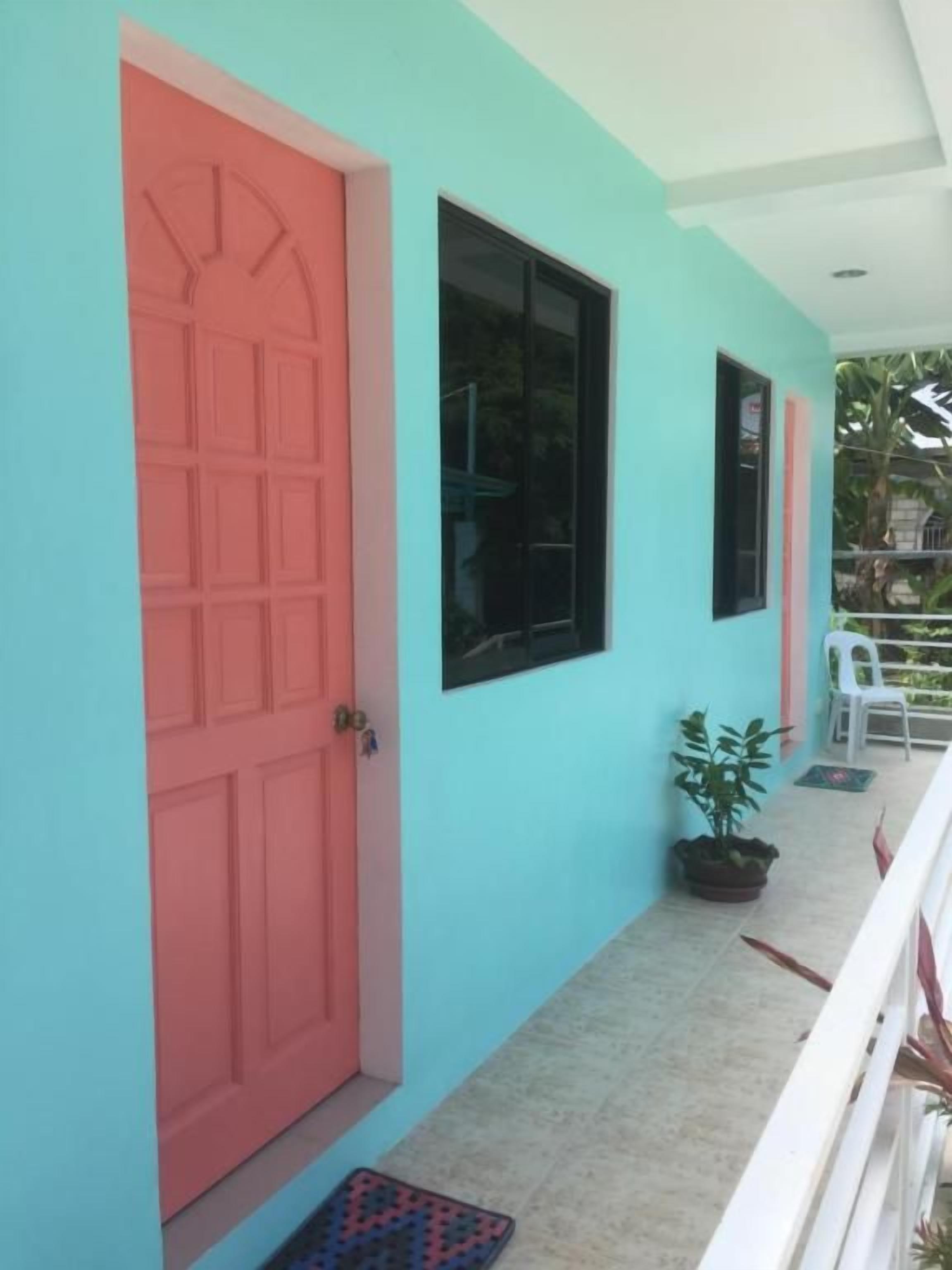 A building exterior with a turquoise wall, a pink door, and a potted plant.