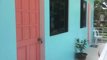 A building exterior with a turquoise wall, a pink door, and a potted plant.