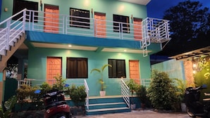 A two-story house with a staircase leading to the upper floor, a balcony, and a motorcycle parked in front.