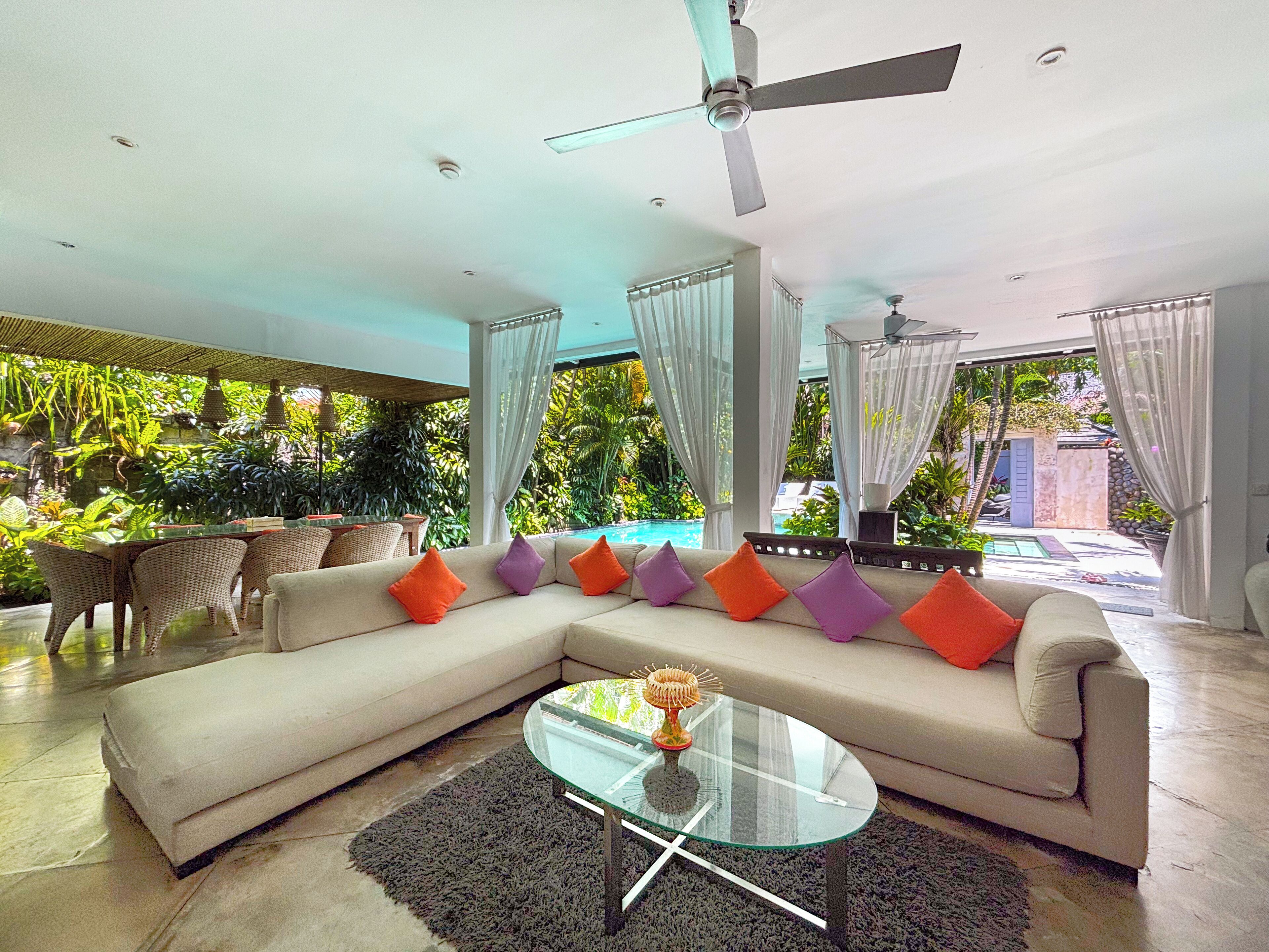 Un salon moderne avec un canapé d’angle beige, une table basse en verre et un ventilateur de plafond.