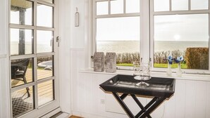 Habitación con ventanas amplias que dan a una masa de agua, una pequeña mesa con un vaso y una vela, y vistas al exterior.