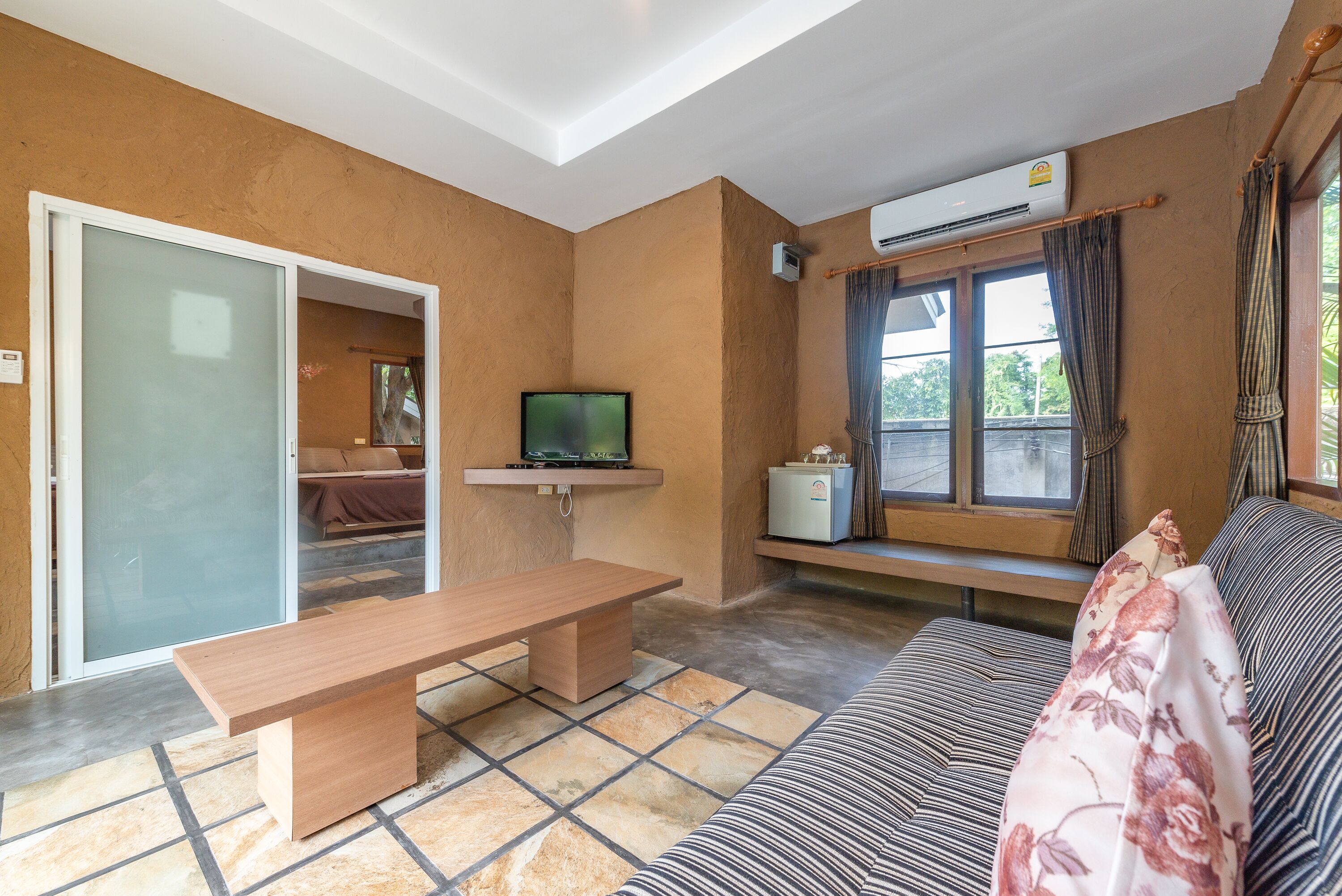 A living room with a wooden bench, a sofa, a television, and a window with curtains.