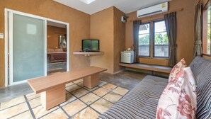 A living room with a wooden bench, a sofa, a television, and a window with curtains. - Muntra Garden Resort (Sattahip)