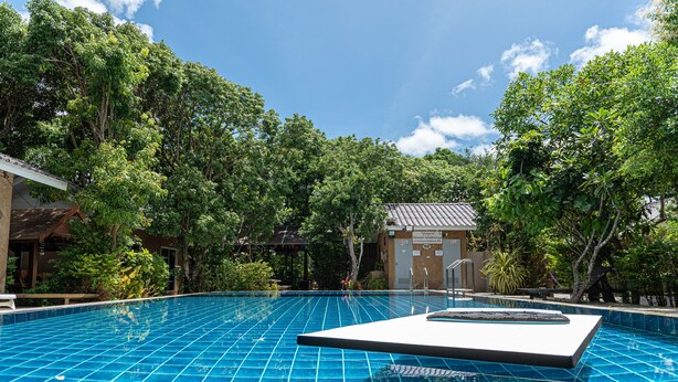 A clear blue pool with a tiled deck, surrounded by lush greenery and trees. - Muntra Garden Resort (Sattahip)