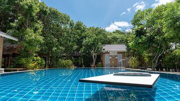 A clear blue pool with a tiled deck, surrounded by lush greenery and trees.