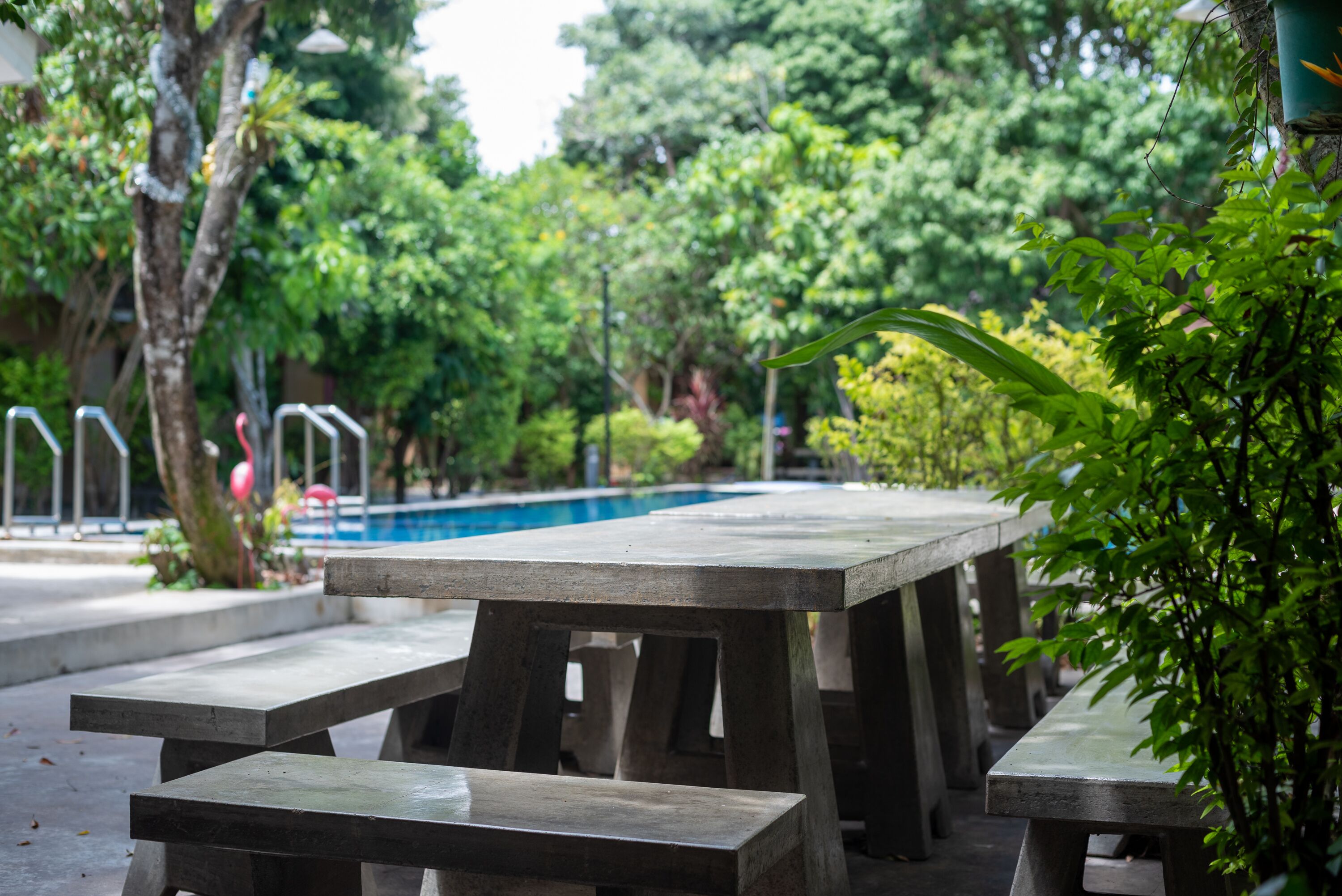 A concrete poolside area with picnic tables and a pool in the background.